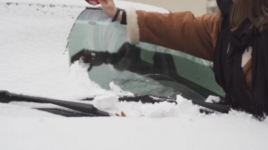 Yolcu arabasının ön camındaki karı temizlerken, genç, diğer taraftaki karı temizlemek için çok uzağa uzanıyor..