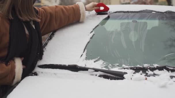 Молодая девушка выгребает снег из лобового стекла автомобиля специальным пластиковым красным треугольником. Первый снег в Люблине. — стоковое видео