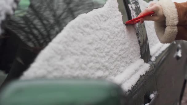 La ragazza pulisce il finestrino laterale sul lato conducente della prima neve mentre cadeva di notte. Una pagaia triangolare rossa con gomma tira neve bagnata. — Video Stock