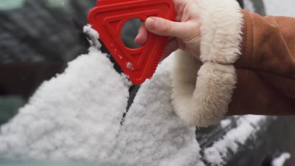 Het meisje veegt de zijruit aan de bestuurderszijde van de eerste sneeuw als het 's nachts viel. Een rode driehoekige peddel met rubber trekt natte sneeuw. — Stockvideo