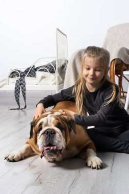 Kız, İngiliz Bulldogs kemerinin yanında yerde oturuyor ve nazikçe eliyle onu okşuyor. İnsan ve köpek.