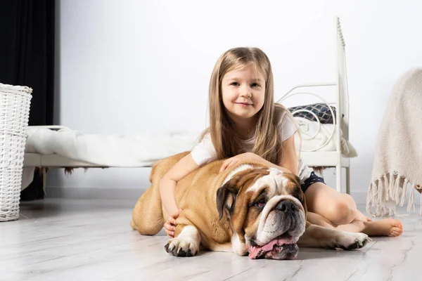 Una joven en un dormitorio, sentada en el suelo con su perro y acariciándolo. Niño y perro. El Bulldog Inglés es un perro de raza pura con un pedigrí. —  Fotos de Stock