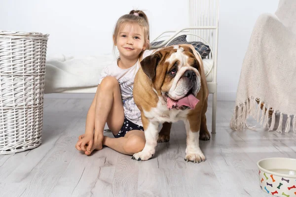 Uma jovem em um quarto, sentada no chão com seu cachorro e acariciando-o. Criança e cão. O Bulldog Inglês é um cão de raça pura com um pedigree. — Fotografia de Stock