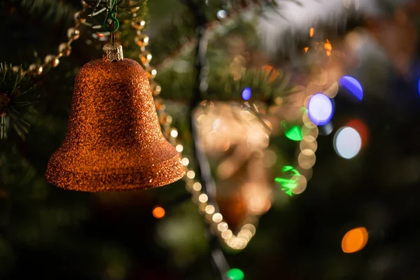 Złoty pomarańczowy dzwon wisi na choince w święta. Świecące lampki choinkowe w tle. — Zdjęcie stockowe