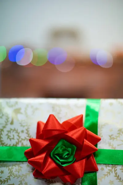 Een geschenk gebonden met een groen lint met een rode strik. Cadeaudoosje met strik. Een cadeautje met Kerstmis. Glanzende kerstboom lichten op de achtergrond. — Stockfoto