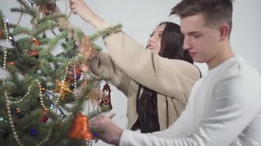 Genç bir çift Noel için bir Noel ağacı süsler. Bir kız ve bir oğlan çam ağacını altın Noel topları ve parlak zincirlerle süslüyor..