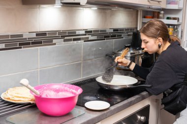 Genç bir kız kısmen pişmiş bir gözlemeyi mutfak spatulasıyla diker ve ters çevirmeye hazırlanır. Ev yapımı krep..