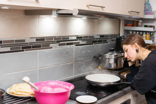 Un adolescente aburrido con panqueques fritos espera ansiosamente a que se fríe la última pieza. Panqueques caseros. — Foto de Stock