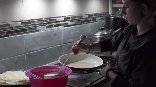 En teenagepige hælder pandekagedejen i en varm gryde med en stor ske. Flydende pandekagedej. Hjemmelavede pandekager. – Stock-video