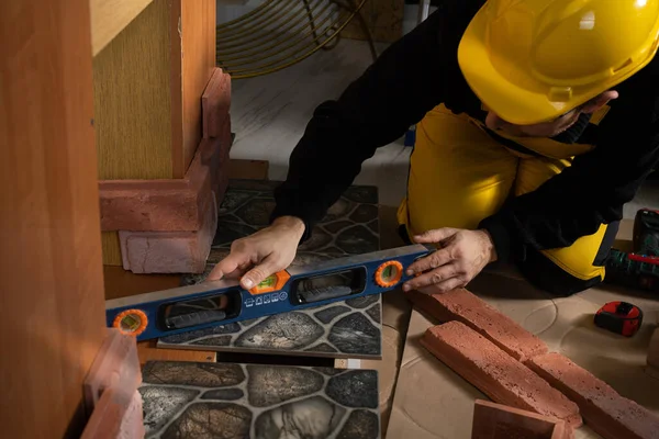 En bygningsarbejder kontrollerer med en spiritus niveau, at terracotta fliser er jævnt placeret i alle områder. Påklædt personlige værnemidler. - Stock-foto