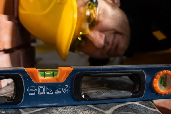 Una vista de cerca de un trabajador de la construcción que comprueba con un nivel de espíritu para ver si la terracota se coloca uniformemente en cada lugar. Vestido con equipo de protección personal. — Foto de Stock