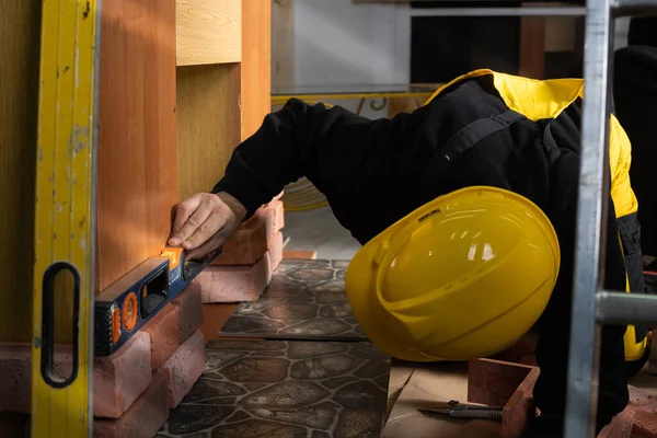 Den manuelle arbejder kontrollerer med et vaterpas, at den dekorative mursten er korrekt placeret. En bygningsarbejder klædt i personlige værnemidler. - Stock-foto