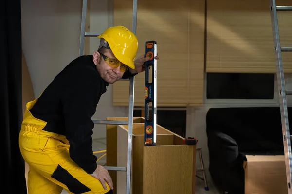 The builder checks with a spirit level that the cabinet is made correctly and without deviations. Construction worker wearing personal protective equipment. — Stock Photo, Image