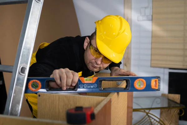 O construtor verifica com um nível de espírito que o gabinete é feito corretamente e sem desvios. Trabalhador da construção civil que usa equipamento de protecção individual. — Fotografia de Stock