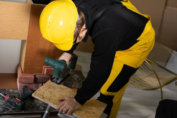 Byggnadsarbetaren klipper träbrädan med ett elektriskt pussel. Under arbetet. Byggnadsarbetare med personlig skyddsutrustning. — Stockfoto