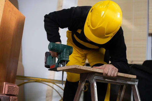 Der Bauarbeiter schneidet das Holzbrett mit einer elektrischen Stichsäge. Während der Arbeit. Bauarbeiter trägt persönliche Schutzausrüstung. — Stockfoto