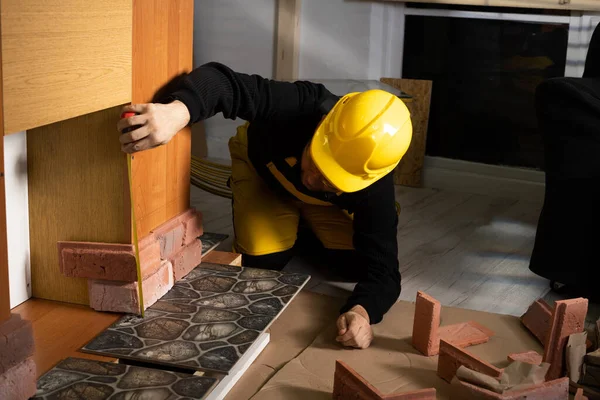 A construction worker in working clothes, kneeling, measures the retractable decorative tiles in the shape of old red brick with a tape measure. — Foto de Stock