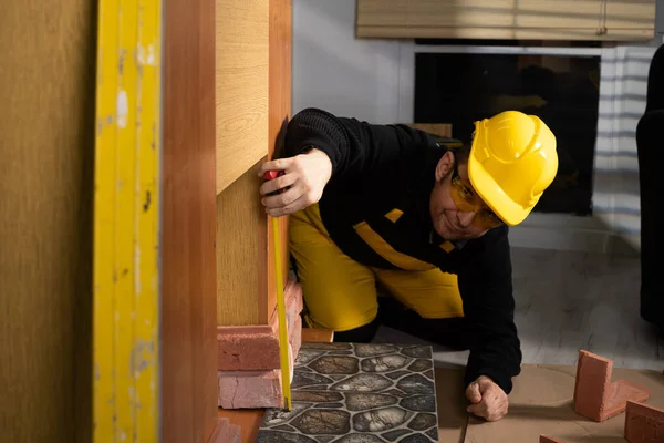 A construction worker in working clothes, kneeling, measures the retractable decorative tiles in the shape of old red brick with a tape measure. — Zdjęcie stockowe