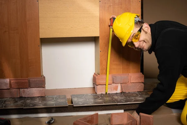 El trabajador de la construcción mira a la cámara y sonríe mientras mide. Usar equipo de protección personal. — Foto de Stock