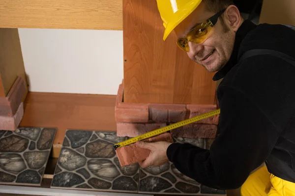 El trabajador de la construcción mira a la cámara y sonríe mientras mide. Usar equipo de protección personal. — Foto de Stock