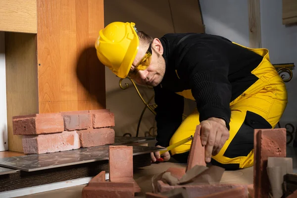 O trabalhador da construção alcança para outra telha decorativa em forma de tijolo para continuar com o trabalho planejado. Trabalhador da construção civil que usa equipamento de protecção individual. — Fotografia de Stock