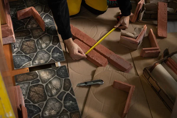 A construction worker in working clothes, kneeling, measures the retractable decorative tiles in the shape of old red brick with a tape measure. —  Fotos de Stock