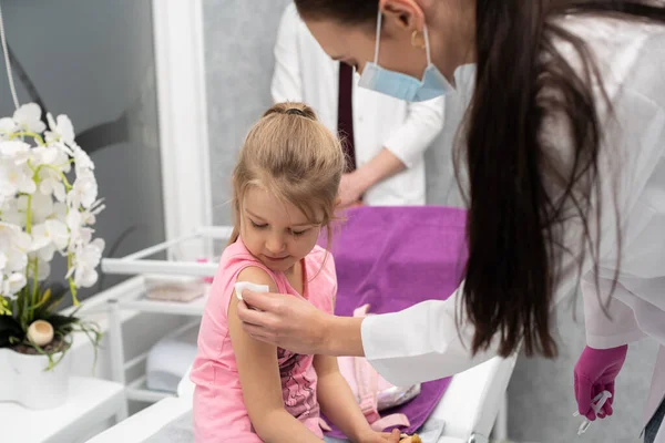 Una joven doctora está preparando a un niño para una inyección desinfectando un pedazo de piel en el brazo con gasa y productos médicos. Vacuna preventiva para niños pequeños. — Foto de Stock