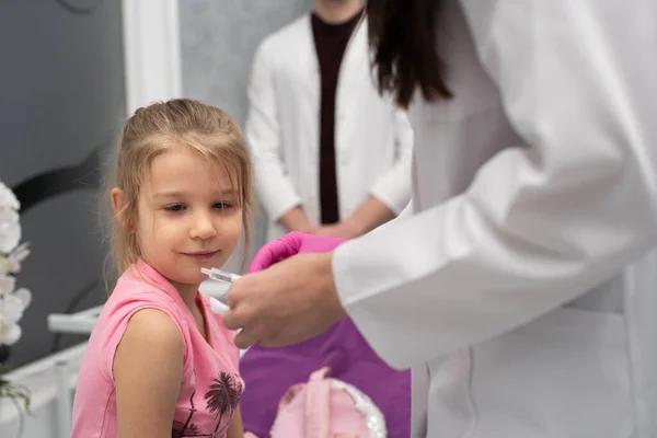 La niña observa con curiosidad mientras el médico prepara la jeringa para la inyección. Vacuna preventiva para niños pequeños. — Foto de Stock