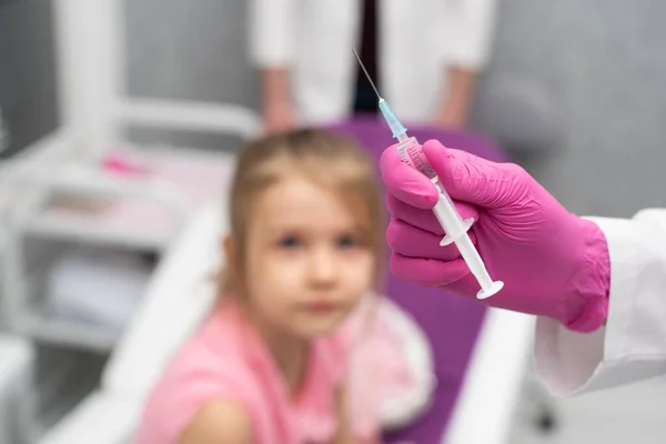 Το κορίτσι παρακολουθεί περιέργως καθώς ο γιατρός ετοιμάζει τη σύριγγα για ένεση. Προληπτικό εμβόλιο για μικρά παιδιά. — Φωτογραφία Αρχείου