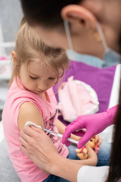 El médico le va a poner una inyección a una niña. El niño mira fijamente en un tazón de estrangulamiento. Vacuna preventiva para niños pequeños. — Foto de Stock