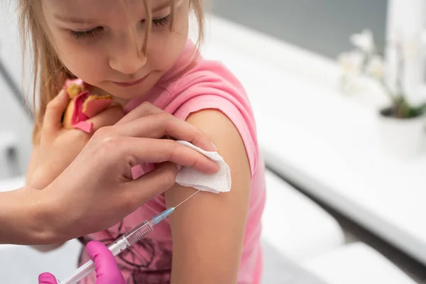 El médico le va a poner una inyección a una niña. El niño mira fijamente en un tazón de estrangulamiento. Vacuna preventiva para niños pequeños. Vista de primer plano. — Foto de Stock