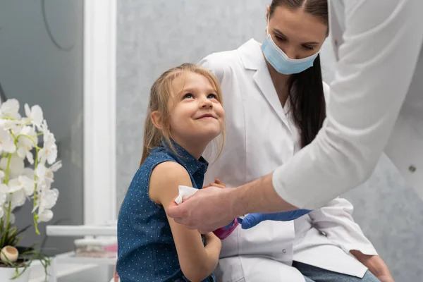 El médico se está preparando para vacunar a una niña. Una enfermera joven se sienta junto al niño para hacer que se sienta seguro. Vacuna preventiva para niños pequeños. — Foto de Stock