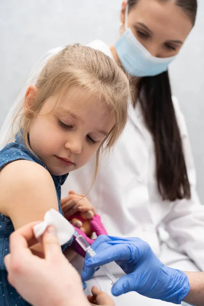 El médico se está preparando para vacunar a una niña. Una enfermera joven se sienta junto al niño para hacer que se sienta seguro. Vacuna preventiva para niños pequeños. — Foto de Stock