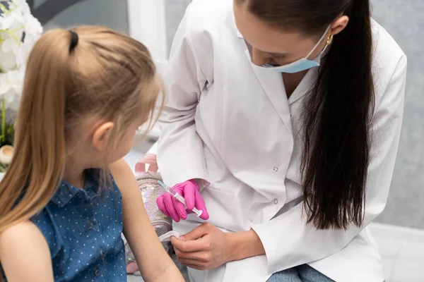 Una enfermera se está preparando para inyectar a una niña con una vacuna previamente preparada. El joven aprendiz intenta hablar con el niño para que no tenga miedo de la inyección. —  Fotos de Stock