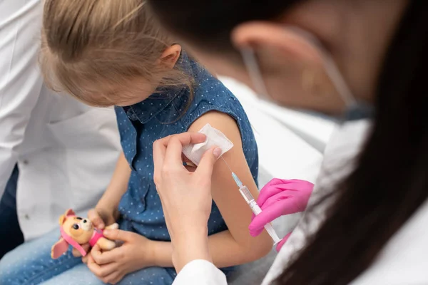 Una enfermera introduce una aguja en el brazo de las niñas con la nueva vacuna. Un médico senior anima a un pequeño paciente durante la vacunación. — Foto de Stock