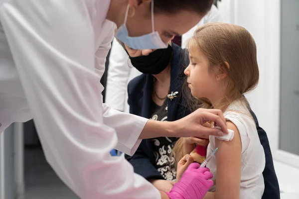 Bir hemşire yeni aşıyla kızların koluna iğne batırıyor. Büyükanne aşı sırasında torununa tezahürat yapıyor. Doktor çocuğun koluna gerekli enjeksiyonu yapar. Önleyici — Stok fotoğraf