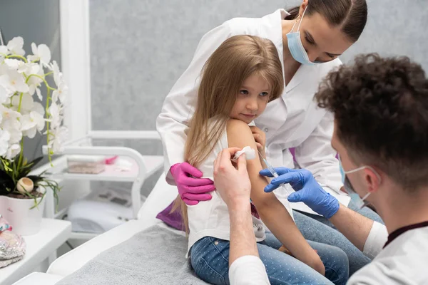 El médico se está preparando para vacunar a una niña. Una enfermera joven se sienta junto al niño para hacer que se sienta seguro. Vacuna preventiva para niños pequeños. — Foto de Stock