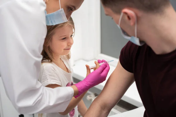 Para animar a la niña, antes de la inyección, la enfermera le sugirió que probara las inyecciones ella misma. Vacuna preventiva para niños pequeños. — Foto de Stock