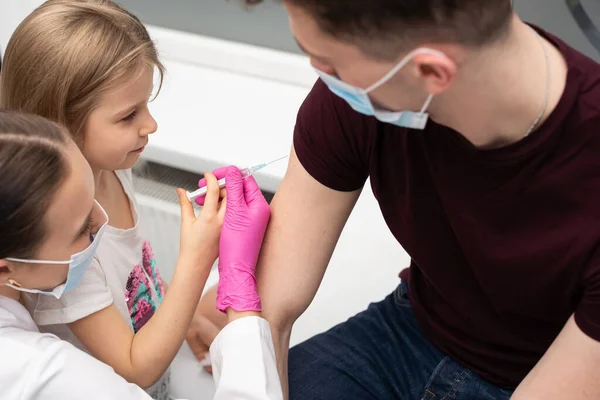 Para animar a la niña, antes de la inyección, la enfermera le sugirió que probara las inyecciones ella misma. Vacuna preventiva para niños pequeños. — Foto de Stock