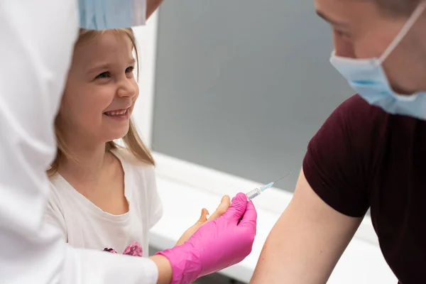 Para animar a la niña, antes de la inyección, la enfermera le sugirió que probara las inyecciones ella misma. Vacuna preventiva para niños pequeños. — Foto de Stock