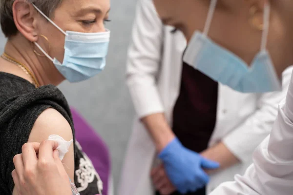 Bir hemşire yaşlı bir kadına aşı yapmaya hazırlanıyor. COVID aşısı 19. Özel bir klinikte steril bir doktor ofisi. Genç bir tıp stajyeri nasıl doğru enjekte edileceğini araştırıyor.. — Stok fotoğraf