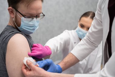 Genç bir stajyer, genç bir yetişkin hastaya COVID19 aşısı yapmayı öğreniyor. Özel bir klinikte steril bir doktor ofisi. Genç bir hemşire, stajyere doğru enjekte etmeyi öğretir..