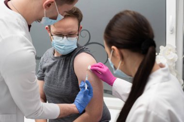 Genç bir stajyer, genç bir yetişkin hastaya COVID19 aşısı yapmayı öğreniyor. Özel bir klinikte steril bir doktor ofisi. Genç bir hemşire, stajyere doğru enjekte etmeyi öğretir..