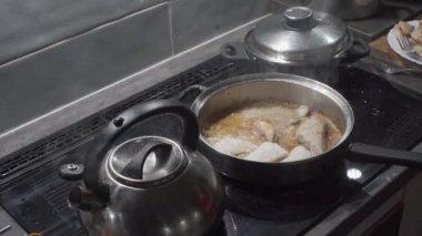 Kadın, kızarmış balık parçalarını tabağa koyar ve kızartma için çiğ parçaları tavaya koyar. Kalın kesilmiş morina parçaları. Ev yemeği..