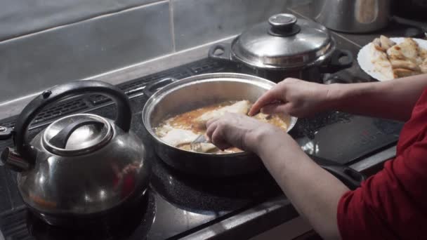 Ενώ τηγανίζει το ψάρι, η γυναίκα γυρίζει τα κομμάτια που τοποθετούνται στο τηγάνι από την άλλη πλευρά. Χοντρά κομμάτια μπακαλιάρου. Σπιτικό μαγείρεμα. — Αρχείο Βίντεο