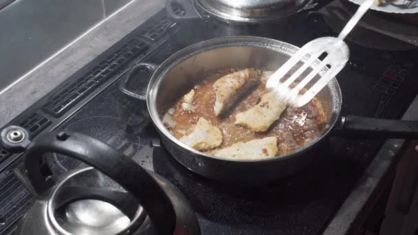 Βγάζουμε τα τηγανητά κομμάτια ψαριού από το τηγάνι, τα οποία τηγανίζονται σε καυτό λάδι. Χοντρά κομμάτια μπακαλιάρου. Σπιτικό μαγείρεμα. — Αρχείο Βίντεο