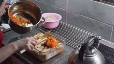 Paslanmaz çelik bir kaba sahip bir kadın, mutfak tezgahının üzerinde duran ısıya dayanıklı cam bir tabakta kalın bir balık tabakasına bir kesik atar ve havuç pişirir. Yunanca 'da balık denilen bir yemek..