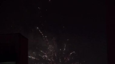 Yeni yıl kutlamaları sırasında gökdelenlerin ana hatlarıyla dolu dar bir çerçeve. Periyodik olarak alevlerden ve diğer havai fişeklerden gelen parlak ışıklar koyu arkaplana çarpıyor