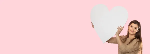 Girl with a large white heart shape in the hands. A student in love stands and holds a large heart shape in her hands. Valentines Day and love. Panoramic frame. — Stock Photo, Image