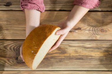 Kadınların elleri, yuvarlak buğdaylı ekmeğin yarısını ahşap tezgahın üzerinde tutar..